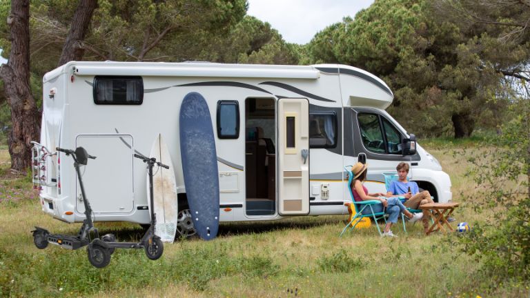 Päarchen vor Wohnmobil im Grünen mit Surfboard und eScootern